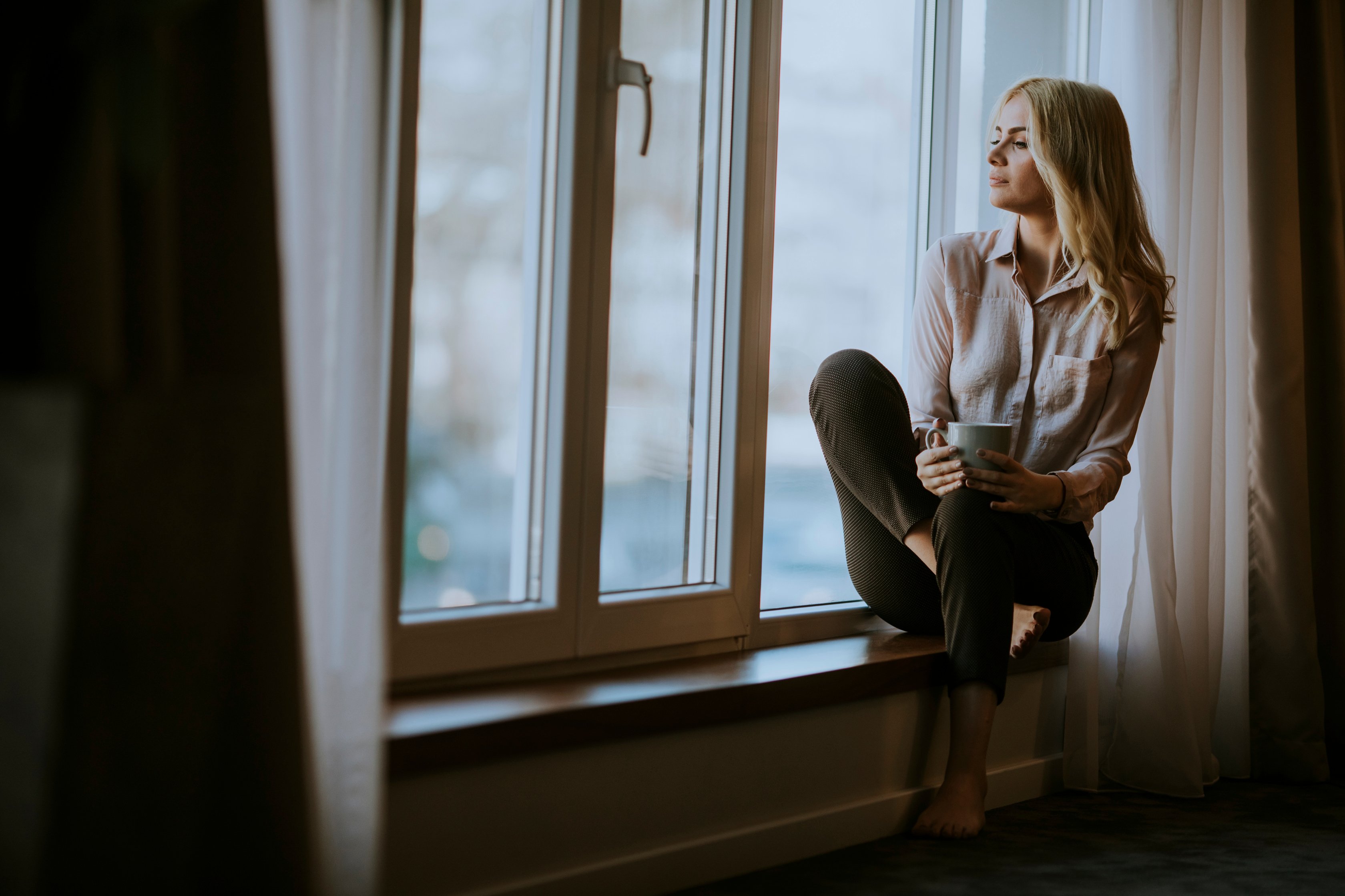 Young Woman with Coffee Sitting on Windowsill